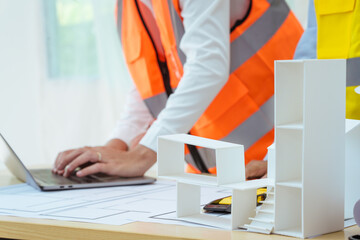 Two young women work at a desk, meticulously designing and drawing plans for building a house. As...