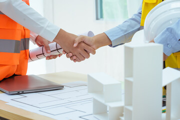 Two young women work at a desk, holding hands while designing and drawing plans for building a...