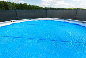 Large expansion pool with a diameter of 3.96 m, located in the yard on the grass, covered with a solar mat.
