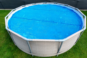 Large expansion pool with a diameter of 3.96 m, located in the yard on the grass, covered with a solar mat.