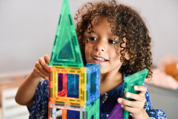 Smiling girl placing green blocks on a colorful tower.