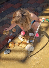 Toddler washing seashells on sunny day