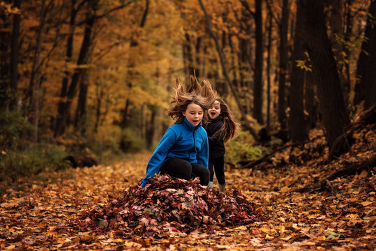 Young sisters jumping in colorful leaf pile in forest