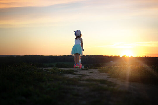 From behind young girl on scooter at sunset