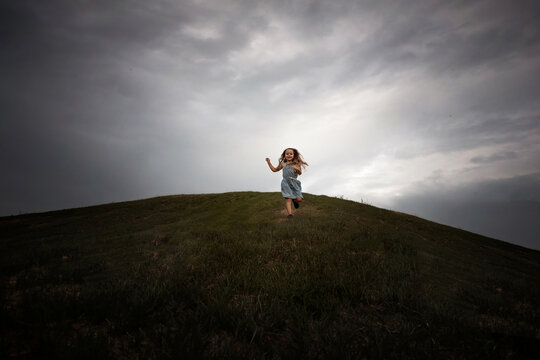 Young girl running down hill under cloudy sky