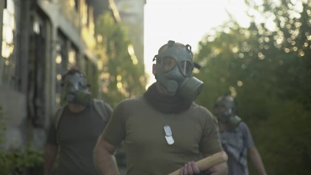 Portrait of a dangerous man with gas mask, the crew in the background, hitting with a baseball bat
