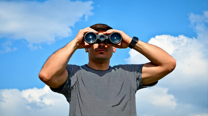 Man Looking Through Binoculars Against Blue Sky, Outdoor Exploration and Adventure Concept, Stock Photograph