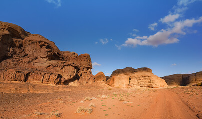 Red orange sandstone rocks formations in Wadi Rum desert, vehicle tire prints in sand road near
