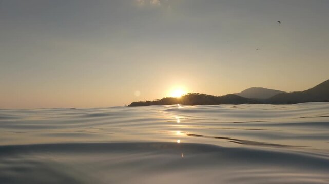 Swimming at sea during sunset, sun setting down behind hills in distance, half camera underwater, dark water visible - thalassophobia concept