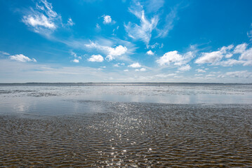 Obraz premium Ebbe am Wattenmeer an der deutschen Nordseeküste bei schönem Wetter,sanften, kleinen Wellen, leichter Brise und aufgelockerter Bewölkung