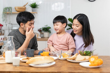 happy family together. Asian parent eating breakfast with little son in the kitchen.