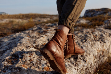 Standing alone on top of a rock in the middle of the day, travel adventure in brown boots
