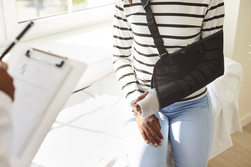 Cropped shot of an African American female patient wearing a black support sling on her broken arm...