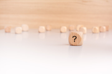 a wooden block with a question mark written on it. many wooden cubes out of focus in the background