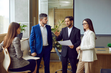 Business team discussing work tasks during a corporate work meeting in the office. Group of people in formal suits talking about current business projects in a modern office workplace