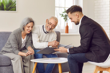 Gray-haired happy smiling senior couple sitting on sofa in the living room at home and having consultation with a male financial advisor about health insurance. Investment in retirement concept