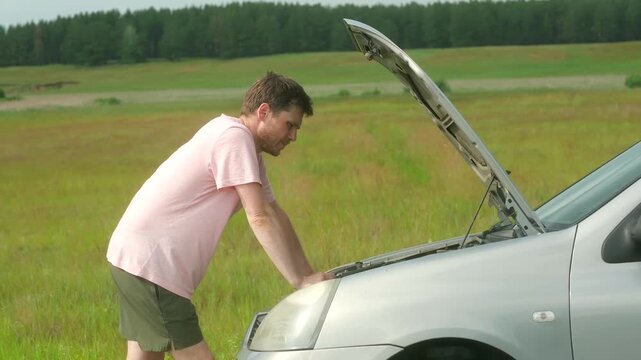 Man checks wires and hoses looking for malfunction. Guy examines engine for visible signs of damage or leaks. Male tries to find source of problem
