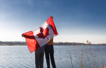 two unrecognizable people holding a large Canadian flag behind their back against the background of...