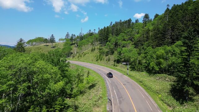 Hokkaido, Japan: Aerial drone footage following cars on the road in the Akan-Mashu National Park with the Mount Oakan volcano in the background in Hokkaido in summer in Japan. 