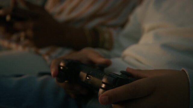 Tilt down shot of black kid and his mother using controller when playing video games sitting on couch at home