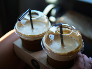 Two cold coffees with black straws in plastic cups stand in cup holders, ready to refresh. These...
