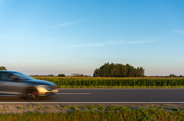 Blurred car driving on countryside road on sunny day. Place for an inscription. Concept of fast transportation, road safety, and rural landscape. High quality photo