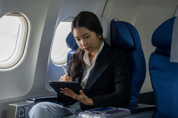 Businesswomen checking business report about financial of new startup project on tablet to analysis strategy and taking notes while sitting near windows during flight business travel in airplane