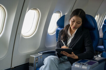 Businesswomen checking business report about financial of new startup project on tablet to analysis strategy and taking notes while sitting near windows during flight business travel in airplane