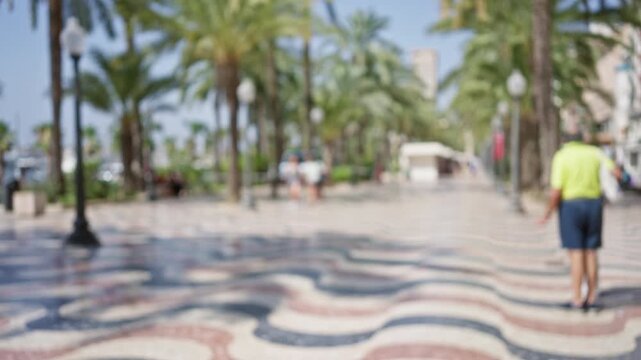 Blurry view of people walking on the colorful wavy pavement of alicante's rambla, lined with tall palm trees under a clear sky.