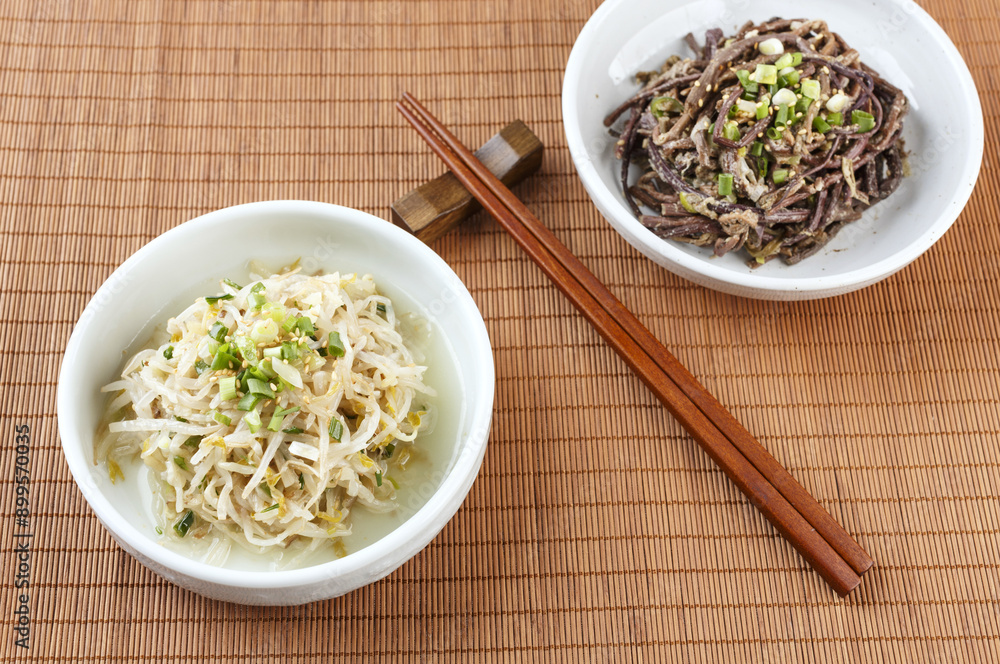 Wall mural Close-up of seasoned bean sprouts and seasoned bracken on two dishes with wood chopsticks on sushi roller mat, South Korea
