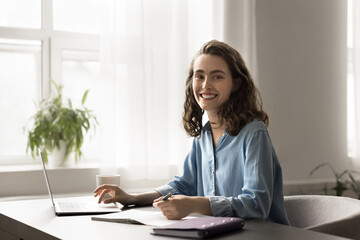 Portrait of intelligent motivated student woman sit at desk with laptop, e-learns using educational website or platform, prepare school essay or task, studying at home. Gain new knowledge, modern tech