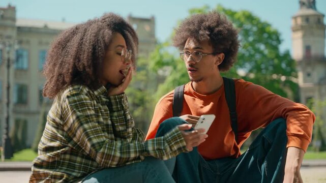 African American students friends woman girl female education man male guy looking mobile phone confused amazed wonder news shock discuss talk outside city friendship university college high school