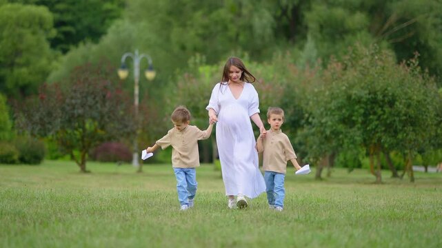 Young Family Picnic Pregnant Mom white dress and Twins.Happy pregnant mom smiles and walks in the park with twins. Green grass and trees. Happy family enjoying summer holidays.
Happy Mom Smile.