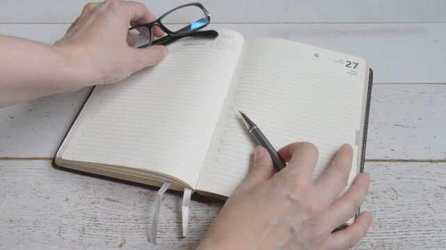 Women's hands remove black glasses, leaf through a notebook and put a pen in it, the concept of working in the office