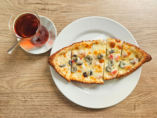 Delicious Turkish sesame bagel pizza made of cheddar cheese, tomato and olives served with hot Turkish black tea on a table. Snack or breakfast concept.