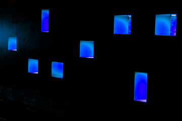 Parede preta com pequenas janelas iluminadas com luz de cor azul. 