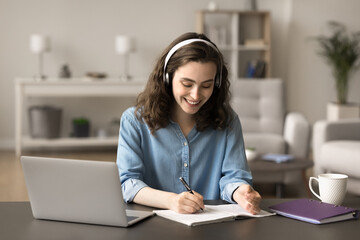 Beautiful smiling student girl makes assignment, listen audio course through headphones, learning...