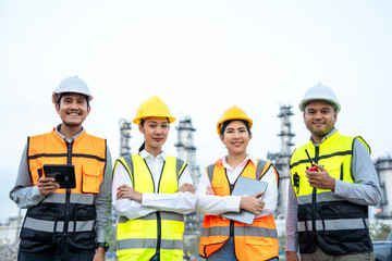 Group of Asian engineer people with safety helmet standing front of oil refinery. Industry zone gas petrochemical. Factory oil storage tank and pipeline. Workers team work in refinery construction
