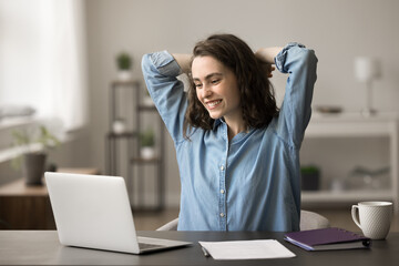 Young freelancer or student woman sit at desk look at laptop screen enjoy on-line project accomplishment, feels satisfied of good job results, put hands behind head, take break after work on computer