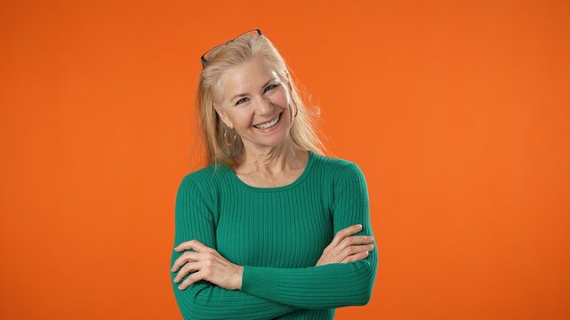 Portrait of blonde successful confident employee business mature woman 50s in green shirt casual clothes look camera isolated on orange background with copy space studio. Achievement career concept.