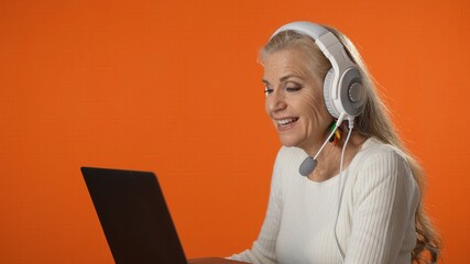 Profile of smiling mature woman wear wireless headset video chat calling on laptop as teacher or...