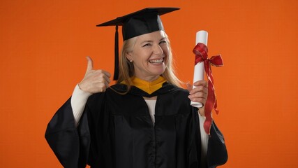 Portrait of happy senior graduate student woman in mortar board with diploma laughing over orange...