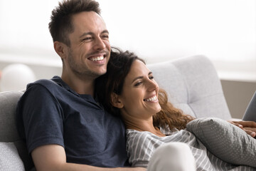 Carefree beautiful Hispanic wife and husband relaxing on sofa laughing while watching comedy movie or stand-up show on tv, spend untroubled pastime at home, look happy and satisfied. Fun. Dating, love