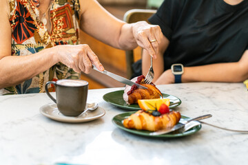 Mother and daughter eating blueberry croissant on dessert table at cafe.