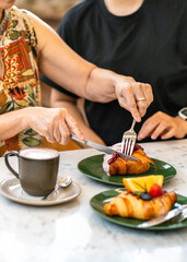 Mother and daughter eating blueberry croissant on dessert table at cafe.
