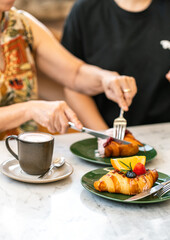 Cup of hot coffee and fruit croissant with blurred mother and daughter eating blueberry croissant on dessert table at cafe.