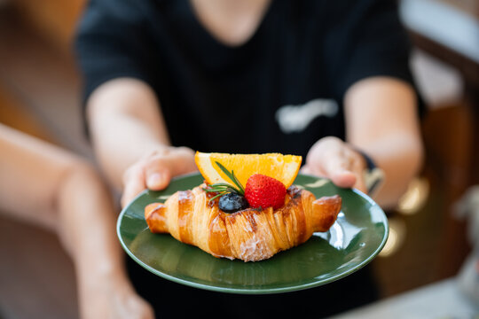 Close up view of woman holding fruit croissant on green plate at cafe