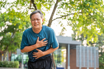Obraz premium Senior asian man tired during jogging at outdoor nature park. Mature asian male intense training workout challenge breathing exhausted. Healthy and activity lifestyle concept.