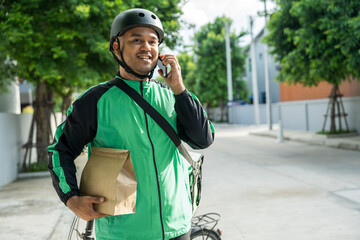 Portrait Rider food delivery man wearing green uniform and helmet cycling a bicycle the food service to customer. Happy delivery man with green backpack shipping of goods to customers.