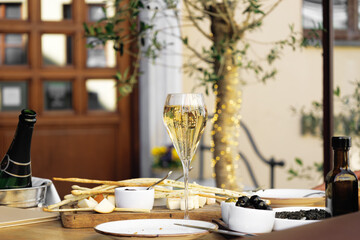 Elegant tall flute of chilled sparkling champagne with different snacks on an elegant formal dining table at outdoor cafe or restaurant in pedestrian street in Europe. Luxury served table at terrace.